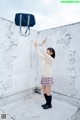 A woman in a school uniform reaching up to catch a bag.