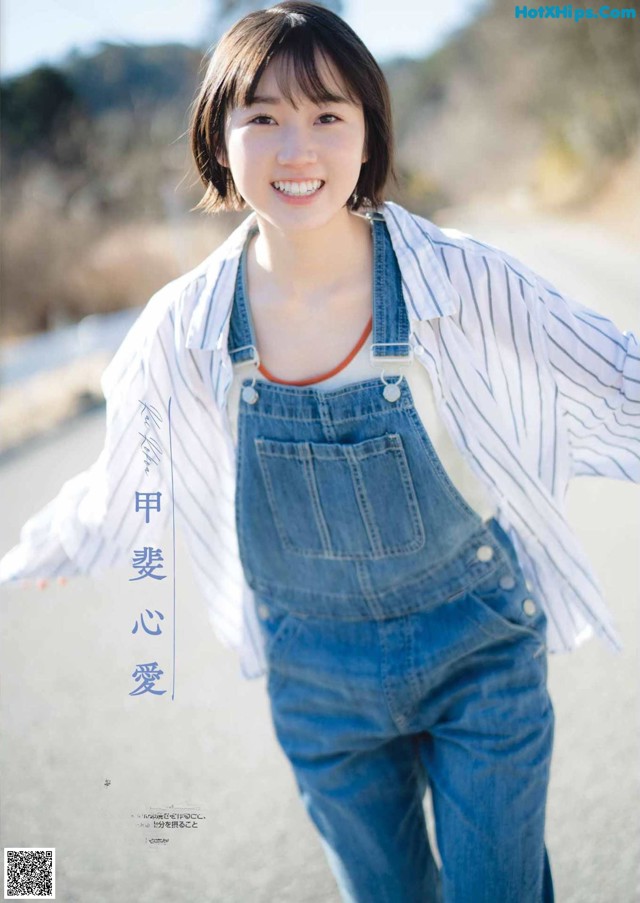 A woman in overalls and a striped shirt smiles at the camera.