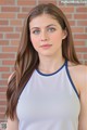 A young woman with long brown hair wearing a white tank top.