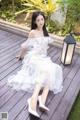 A woman in a white dress sitting on a wooden deck.