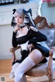 A woman in a maid outfit sitting on a chair.