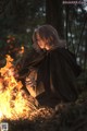 A woman sitting in front of a fire in the woods.